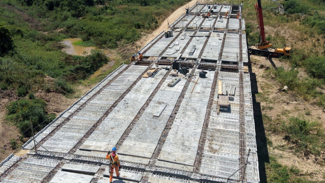 Estrutura de viaduto em construção vista do alto com trabalhadores e equipamentos em área de vegetação. Estrutura de viaduto em construção vista do alto com trabalhadores e equipamentos em área de vegetação.