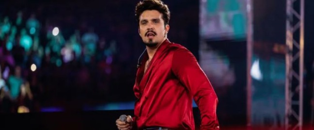 Cantor se apresenta no palco, segurando microfone durante show diante do público.