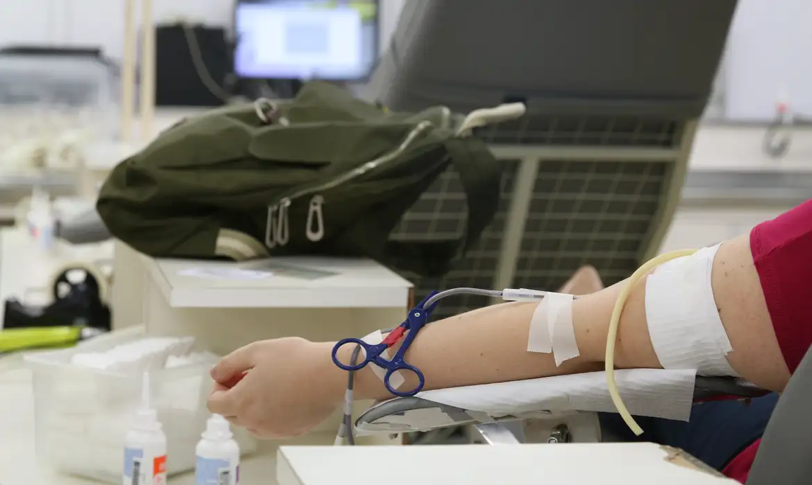 Pessoa realiza doação de sangue com braço conectado a equipamento de coleta