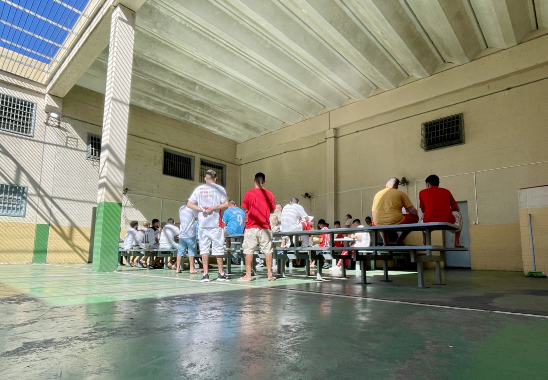 Sentados sobre as mesas e bancos do pátio da Galeria A, apenados assistem à missa (Foto: Júnior Posselt/Folha do Mate)